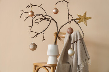 Christmas decoration with tree branches and festive balls in white vase on beige wall background