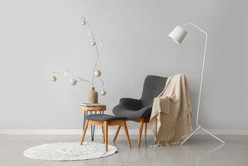 Armchair and table with Christmas decor near grey wall in room