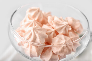 Glass bowl with tasty meringues on light background, closeup