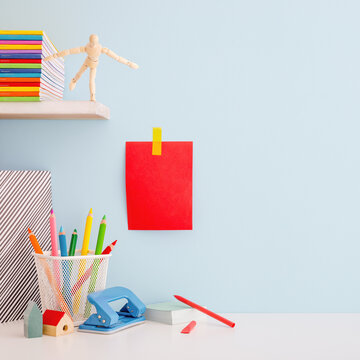 Creative desk full of school accessories and red note on blue wall. Learning workspace.	
