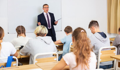 Man teacher with notebook is giving interesting lecture for students in the classroom