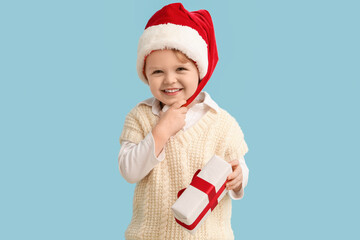 Little boy in Santa hat and with Christmas gift on color background