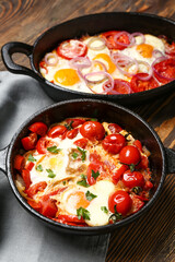 Baking dish and frying pan with tasty Shakshouka on wooden background