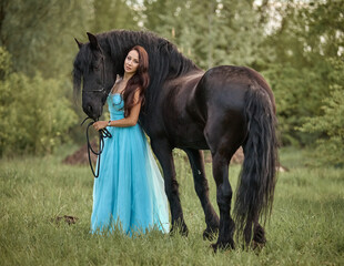 Beautiful long-haired girl in a dress next to a black horse