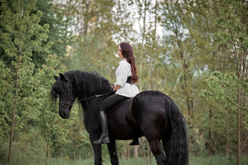 Beautiful long-haired girl riding a Friesian horse