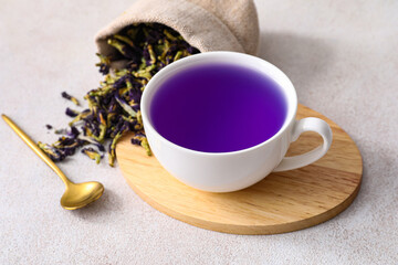 Cup with organic blue tea and bag with dried butterfly pea flowers on light background