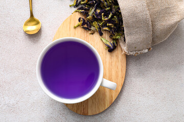 Cup with blue tea and bag with dried butterfly pea flowers on light background