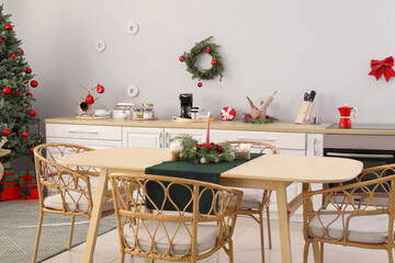 Dining table with burning candle and fir branches in kitchen decorated for Christmas