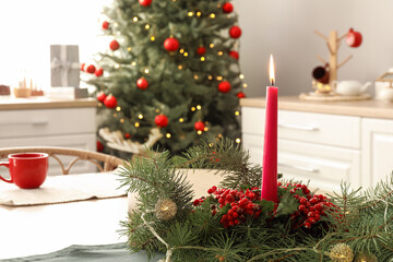 Burning candle with rowan and fir branches on dining table in kitchen