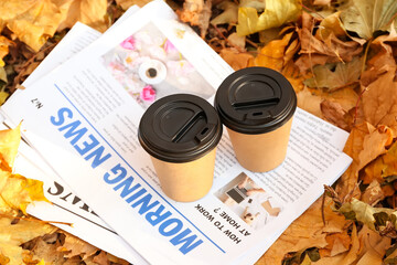 Takeaway cups of tasty coffee and newspapers on fallen leaves in autumn park