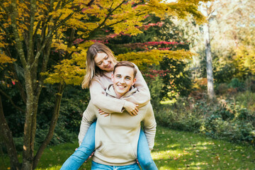 Young caucasian couple in love having fun during a walk in nature. Happy woman enjoying a piggyback...