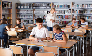 Obraz premium Diligent efficient glad schoolchildren preparing for lesson in school library, reading and writing