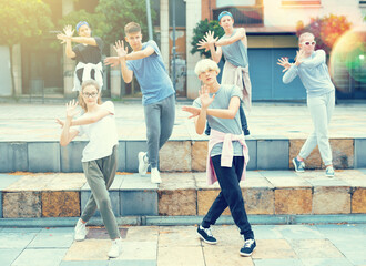 Confident teen boys and girls dancing modern choreography on city street on summer day.