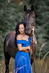 Obraz premium Beautiful long-haired girl in a blue dress with a brown horse