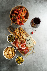 traditional Spanish or Italian tapas. jamon iberico, blue cheese, crackers, olives, grapes and dry red wine,  grey stone background. Top view