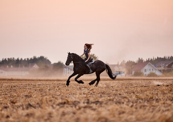Girl riding a friesian horse in a field at sunset