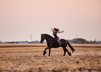 Girl riding a friesian horse in a field at sunset