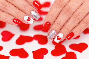 Beautiful female hands with romantic manicure nails, red gel polish, hearts and Valentine's day design