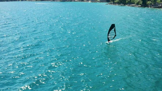 Drone spins around person standing on a sailboard. Windsurfing in the open sea