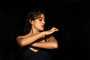 Portrait of a Latin woman crossing her arms while standing on a black background. Female body expression concept.