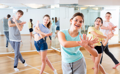 Fototapeta premium Positive teen girl exercising in group with friends during dance class