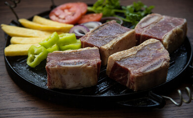 BEEF CUT INTO PIECES, WITH VEGETABLES SUCH AS TOMATO, ONION, PARSLEY, PEPPERS AND POTATOES, ON GRILL, READY TO BRING TO THE FIRE