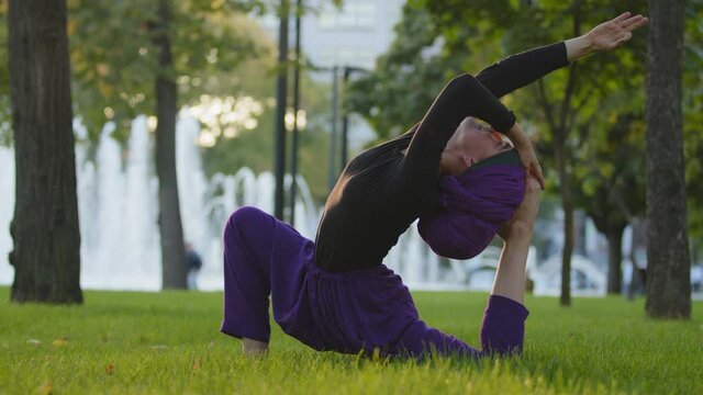 Muslim islamic girl in hijab trainer guru yoga master woman doing stretching exercises in park on green grass doing sports sits in beautiful acrobatic pose asana with back bend stretch on lawn outdoor