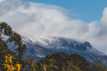 Snow on the mountain tops and clouds rolling over the thick vegetation shot in Tasmania, Australia