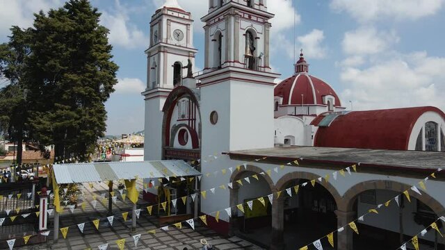 Church in State of Mexico on the day with blue sky and white clouds, cinematic aerial footage with drone in a small town with decoration of tematic party of saints