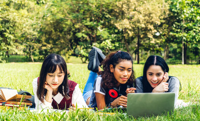 Group of smiling international student or teenager sitting and learning using laptop computer doing their homework with read book together in park at university.Education and friendship Concept