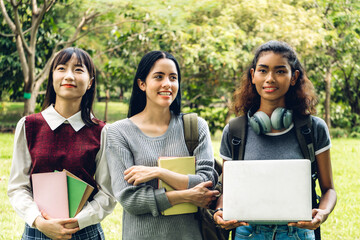 Fototapeta na wymiar Smiling woman international student or teenager standing and holding book look at camera with group of student in park at university.Education and friendship Concept
