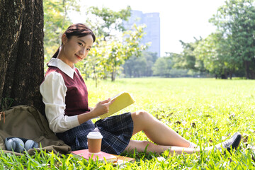 Naklejka na ściany i meble Portrait of beauty student or teenager asian woman read the paper book work study and learning looking at page magazine while sitting in park at university.Education
