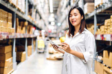 Portrait of smiling asian engineer woman order details on tablet computer for checking goods and supplies on shelves with goods background in warehouse.logistic and business export