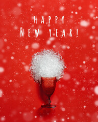 Red glass from which snow scattered, winter holidays concept, New year, Christmas party. Colored glassware trend wine glass on red with snowing and text happy new year.