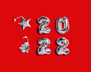 New Year 2022 silver balloons number and  decorations form as Christmas tree and silver star on red fabric background with copy space