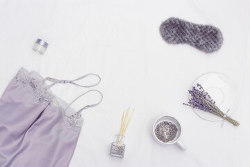 Sleep mask, silk pajamas, aroma balsam, dry lavender flowers on white bedclothes. Concept healthy dream.