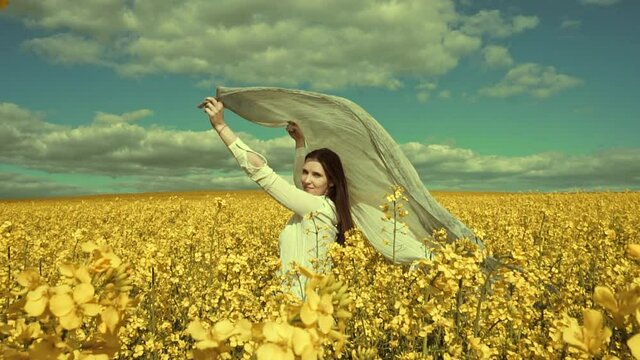 Beautiful woman with wind fluttering scarf in the rapeseed field. Woman freedom. Women rights.
