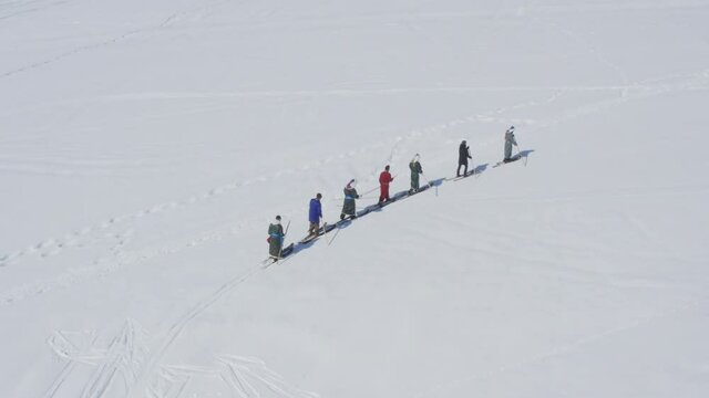 Skiers in traditional Tuva robes walking on fur skis in snow, aerial drone view winter