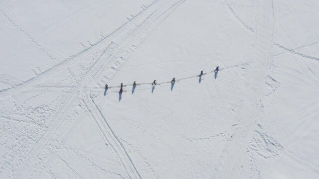 Skiers walking in single line formation in snow, aerial top down view