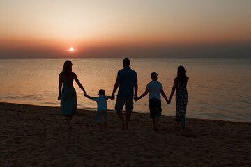 big family on the beach. Silhouettes of people against the sunset. 5 people holding hands