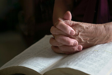 Close up view of senior woman praying, hands folded on top of bible.