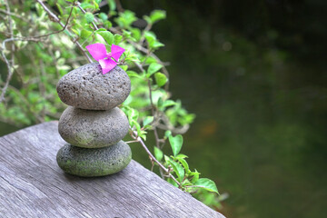 Fototapeta na wymiar Stones stacked on top of each other, next to nature flowers and pond.