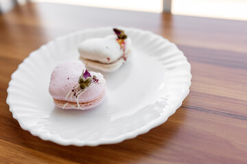A pink heart-shaped cake lies on a white plate on a light background. Light macaroons on a white canvas. Valentine's Day background