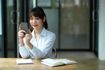 Female employee relaxes in her office by using her modern smart phone.