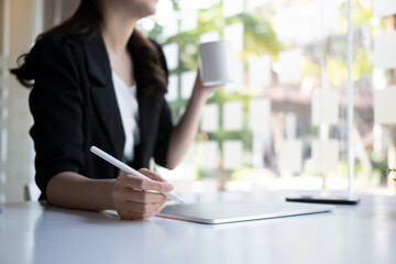 Cropped shot thoughtful business woman drinking coffee and using digital tablet in office.