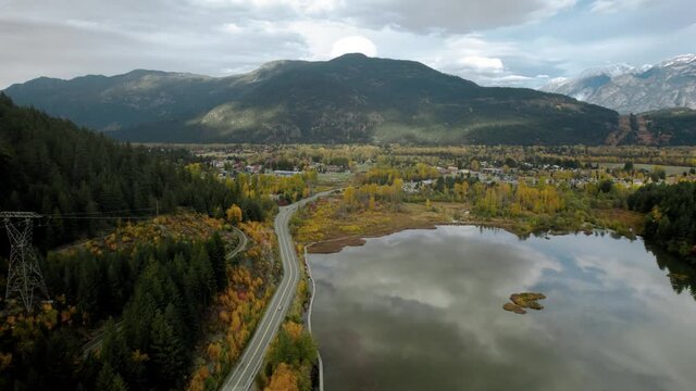 Cinematic Tracking Drone Shot of Mountain Village with Car on Highway Next to Lake in Fall British Columbia, Canada (4K)