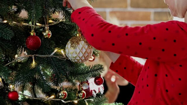 Child hands decorate Christmas or New Year fir tree with sphere toys. Kid carefully straightens and put white ball. Small girl hangs and putting Christmas decoration on festive decorated fir tree