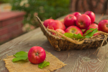 Fototapeta na wymiar Ripe red apples in a wicker basket on a wooden table.