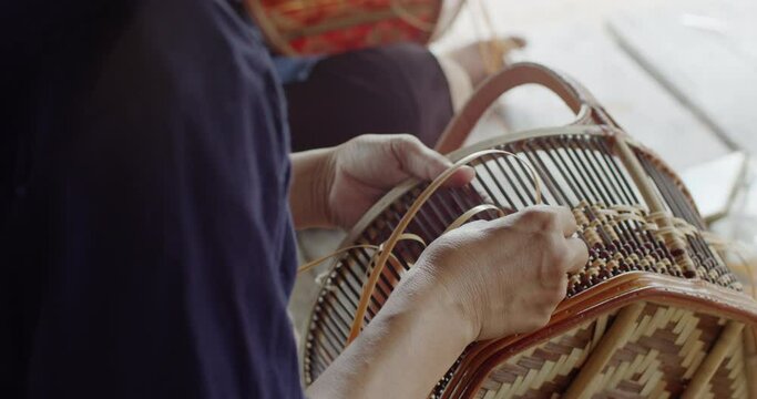  2 Thai female farmers weave basket in traditional Thai art patterns to sell as extra income in countryside of Thailand.	