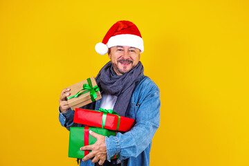 latin senior man holding Christmas presents with santa hat on yellow background in Mexico Latin America